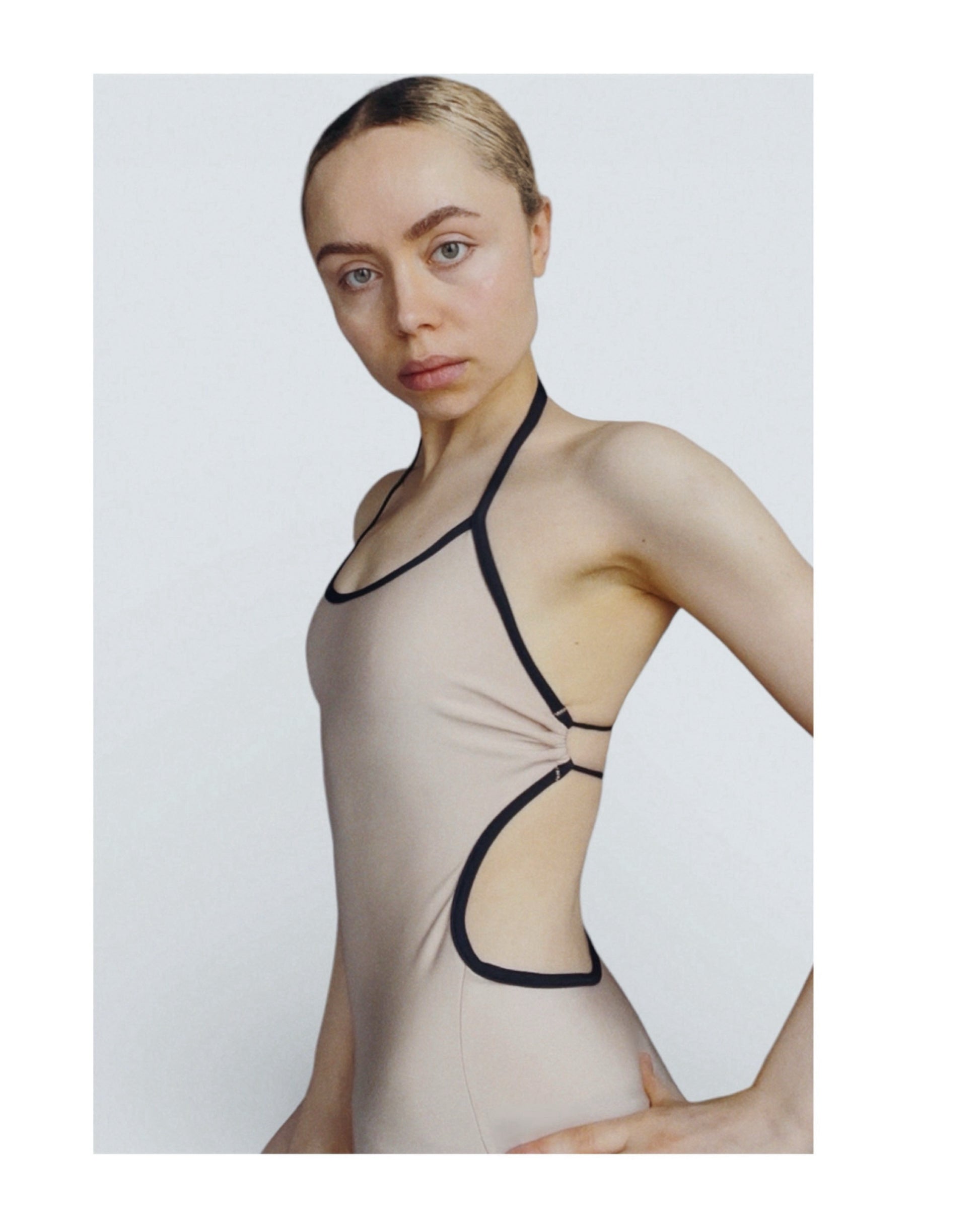 Woman wearing a beige bodysuit with black straps on a white background